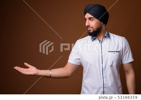 Young bearded Indian Sikh man wearing turban against brown backg Young bearded Indian Sikh man wearing turban against brown backg 53166359