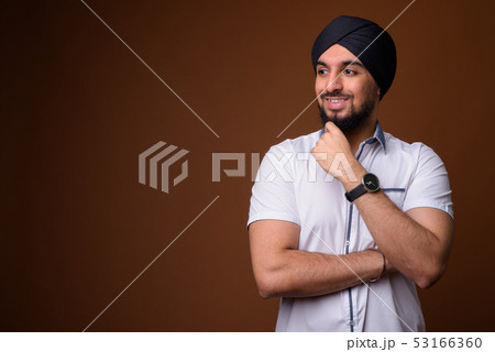 Young bearded Indian Sikh man wearing turban against brown backg Young bearded Indian Sikh man wearing turban against brown backg 53166360