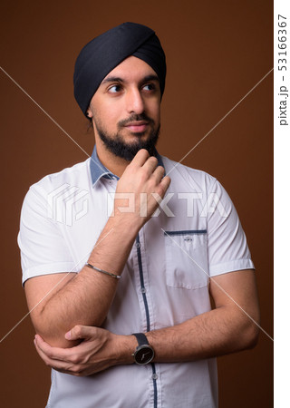 Young bearded Indian Sikh man wearing turban against brown backg 53166367