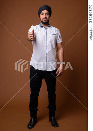 Young bearded Indian Sikh man wearing turban against brown backg 53166370
