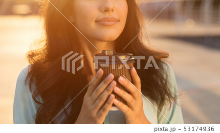 Girl smelling hot chocolate in takeaway cup, outdoors Girl smelling hot chocolate in takeaway cup, outdoors 53174936