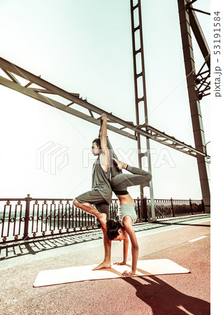 Barefoot female yogi and her partner exercising outdoors Barefoot female yogi and her partner exercising outdoors 53191584