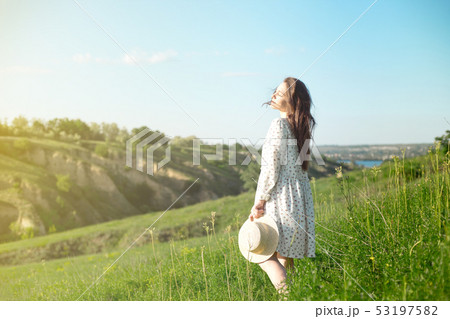Beautiful sensual brunette in dress and hat standing with eyes closed in nature in bright back lit 53197582