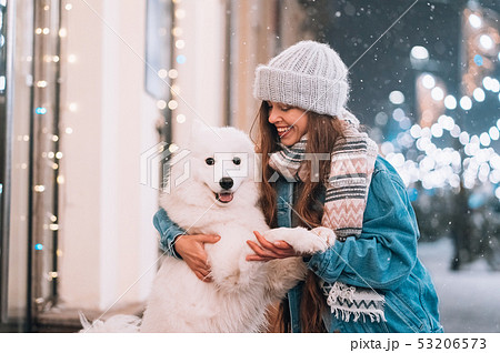 A woman is hugging her dog on a night street. 53206573