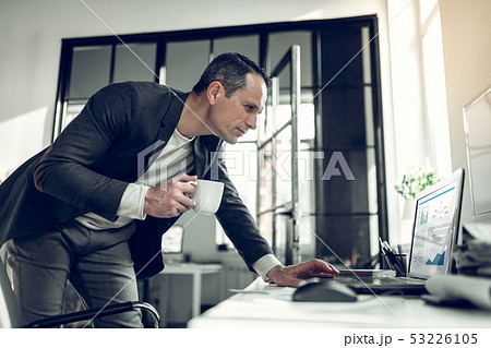 Businessman holding cup of coffee reading e-mail on laptop 53226105