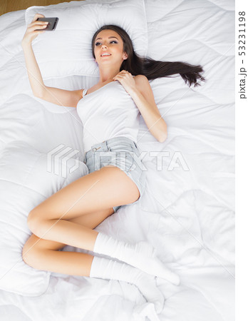Happy morning. Portrait of a smiling pretty young brunette woman relaxing in white bed 53231198