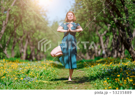 Photo of woman with closed eyes in long green dress doing yoga in forest 53235889