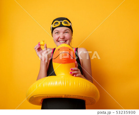 Image of smiling woman in bathing suit with lifebuoy on empty orange background 53235930