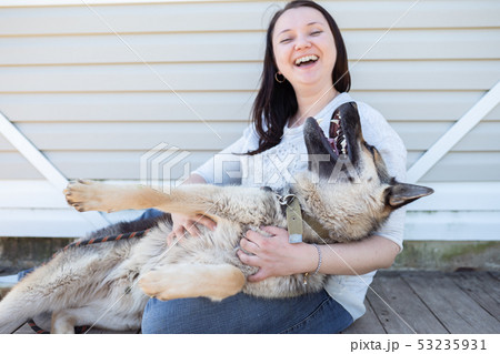 Photo of smiling woman in jeans and white jacket sitting next to happy shepherd puppy against white 53235931