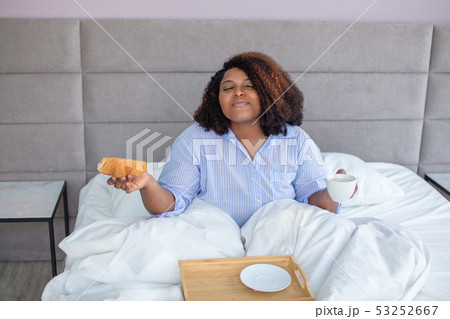 African american woman enjoys breakfast while sitting in the bed 53252667
