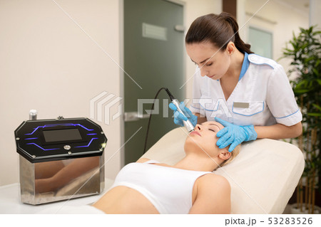 Dark-haired dermatologist doing laser skin treatment for woman 53283526