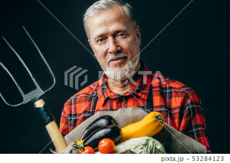 old garderner is holding vegetables and pitchfork 53284123