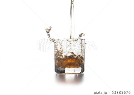 Whiskey pouring into glass with ice on light 53335676