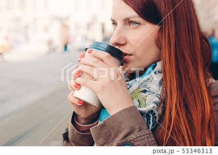 Beautiful redhead girl posing on the street in cold weather, she has coffee cup. Red manicure 53346313
