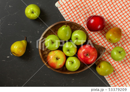 Tabletop photo - apples and pears in wooden carved bowl on black marble effect working desk with red 53379209