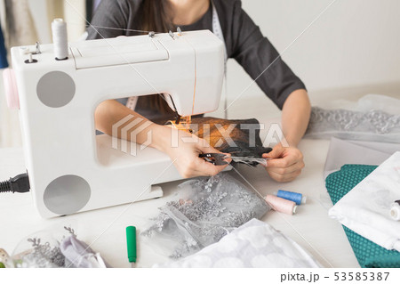 people, fashion and showroom concept - young fashion designer sews clothes on a sewing machine close 53585387