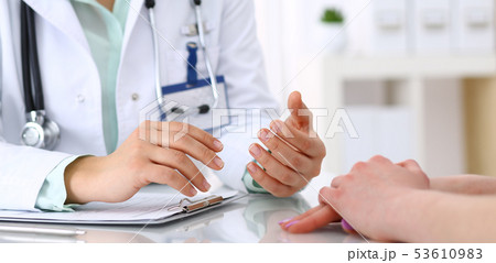 Doctor and patient talking while sitting at the desk in hospital office, close-up of human hands Doctor and patient talking while sitting at the desk in hospital office, close-up of human hands 53610983