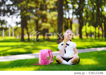 Little school girl with pink backpack sitting on grass after lessons and thinking ideas, read book 53613296