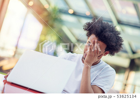 Serious Afro American male student in T-shirt sitting at cafeteria drinking takeaway coffee working Serious Afro American male student in T-shirt sitting at cafeteria drinking takeaway coffee working 53625134