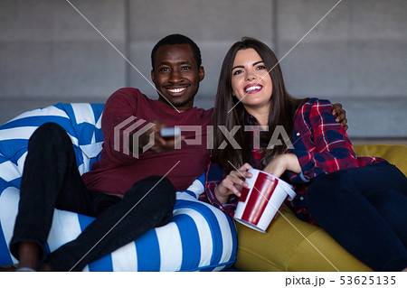 Portrait of young couple sitting on sofa watching a movie with expression on their faces Portrait of young couple sitting on sofa watching a movie with expression on their faces 53625135