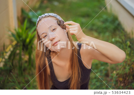 A young woman makes a face mask with snail mucus. Snail crawling on a face mask 53634423