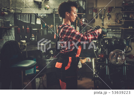 African american woman mechanic repairing a motorcycle in a workshop African american woman mechanic repairing a motorcycle in a workshop 53639223