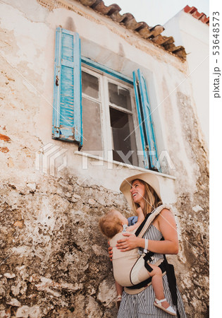 A young mother with a baby in a carrier walking in town on summer holiday. A young mother with a baby in a carrier walking in town on summer holiday. 53648573