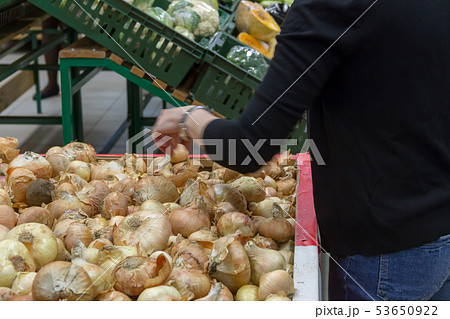 the girl chooses onions on a counter of shop 53650922