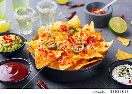 Nachos chips with melted cheese and dips variety in black bowl. Grey stone background. Close up. 53652318