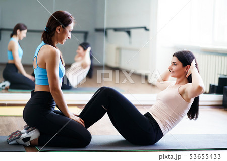 woman doing sit-up with fitness instructor support 53655433