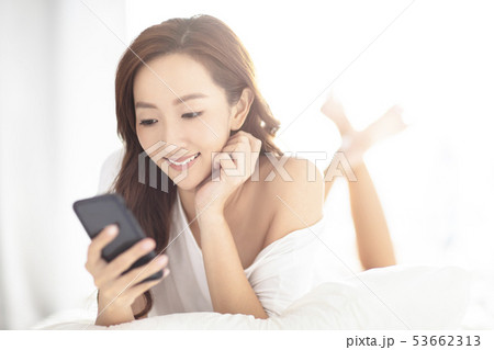 young smiling woman watching mobile phone on bed young smiling woman watching mobile phone on bed 53662313