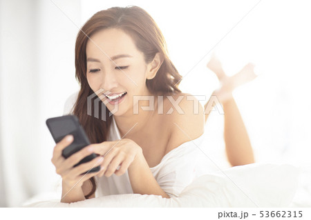 young smiling woman watching mobile phone on bed 53662315