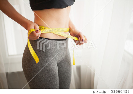 Hands measuring waist with a tape. Slim and healthy woman at her home 53666435