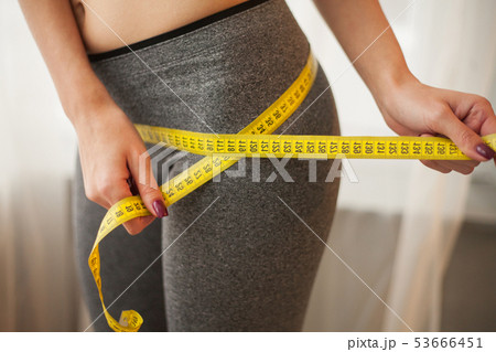 Hands measuring waist with a tape. Slim and healthy woman at her home 53666451