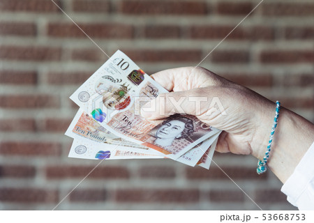 Woman holding pounds sterlings against brick wall background 53668753