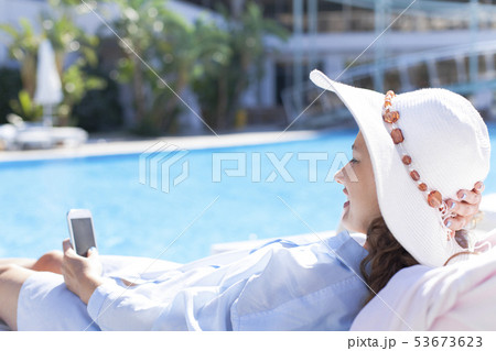 Woman using mobile phone by the pool Woman using mobile phone by the pool 53673623