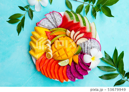 Tropical fruits assortment on a plate with frangipani flowers. Blue background. Top view Copy space. Tropical fruits assortment on a plate with frangipani flowers. Blue background. Top view Copy space. 53679949