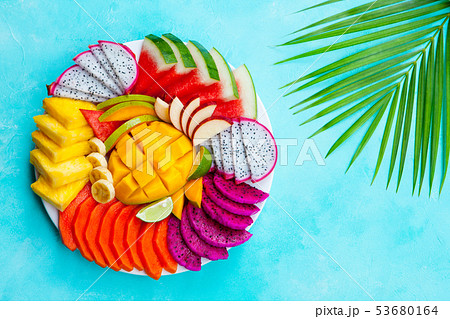 Tropical fruits assortment on a white plate with palm leaf. Blue background. Top view. Copy space. Tropical fruits assortment on a white plate with palm leaf. Blue background. Top view. Copy space. 53680164