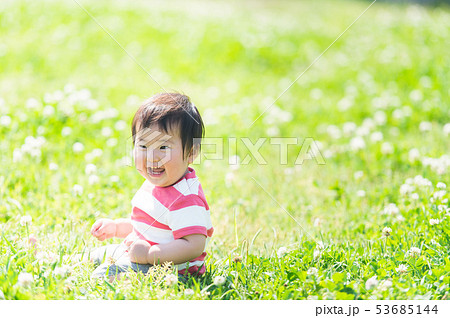芝生で笑顔でお座りする赤ちゃん 乳児 の写真素材