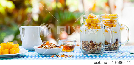 Mango, yogurt, granola dessert, breakfast in jars. Tropical outdoor background. Copy space. 53686274