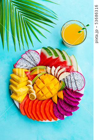 Tropical fruits assortment on a white plate with mango smoothie, juice. Blue background. Top view. 53686316