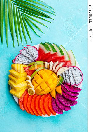 Tropical fruits assortment on a white plate with palm leaf. Blue background. Top view. 53686317