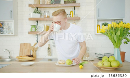 Blonde man is drinking coffee while having breakfast at the kitchen 53686380