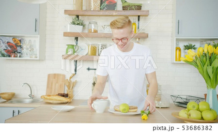 Beautiful blonde man is making breakfast for his girlfriend in the morning at the kitchen Beautiful blonde man is making breakfast for his girlfriend in the morning at the kitchen 53686382