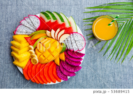 Tropical fruits assortment on a white plate with fresh juice. Grey background. Top view. Copy space. 53689415