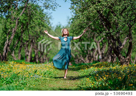 Full-length photo of woman with closed eyes and raised hands in long green dress doing yoga in 53690493