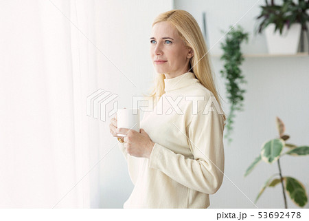 Middle-Aged Woman Drinking Coffee And Looking Through Window Middle-Aged Woman Drinking Coffee And Looking Through Window 53692478