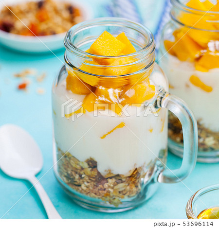 Healthy breakfast, dessert. Fresh mango fruit with yogurt and granola in jars. Blue background. 53696114