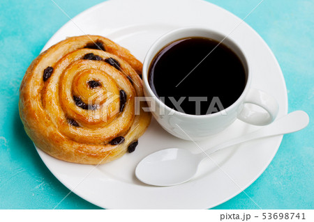 Fresh danish pastry with raisins with a cup of black coffee on blue table background. 53698741