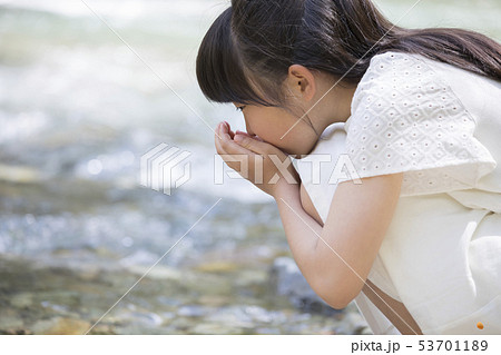 川の水を飲む白いワンピースを着た少女 夏イメージ ミネラルウォーター広告イメージの写真素材